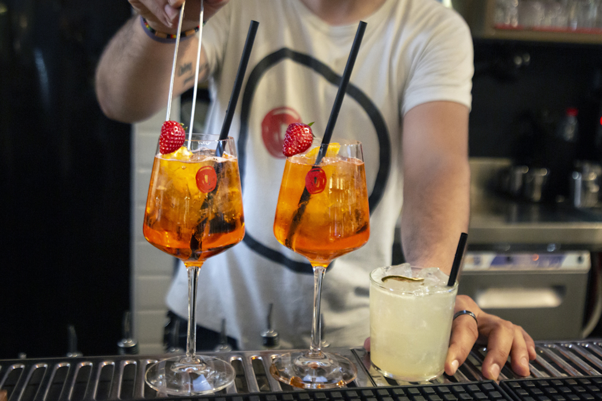 Un cantinero que prepara un cóctel de color naranja brillante con vasos de tallo alto