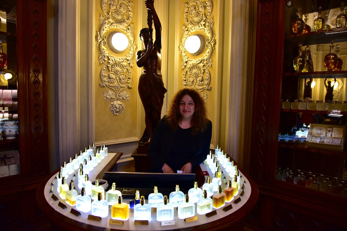 Una mujer se para en un mostrador rodeada de coloridos frascos de perfume.