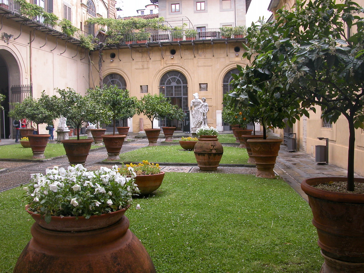 Patio dentro del palacio renacentista con pasarelas de piedra y grandes macetas con plantas