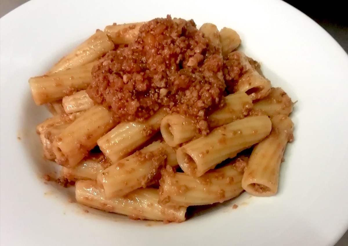 Pasta rigatoni con salsa de carne en un plato blanco.