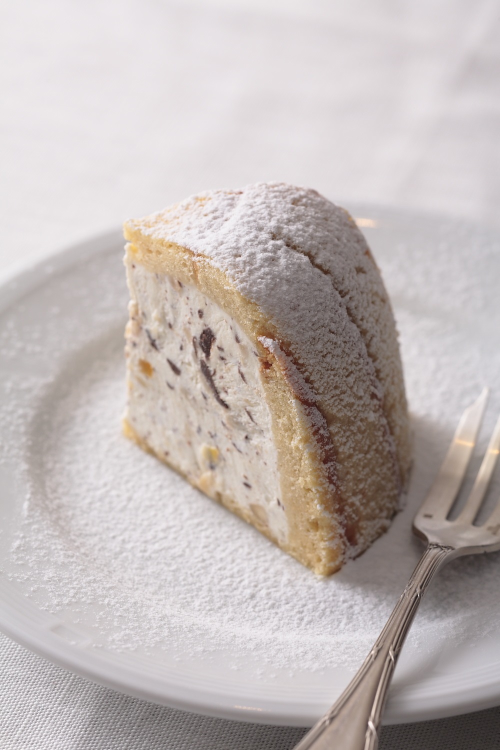 Una rebanada de pastel de cúpula redonda con relleno y azúcar glas con un tenedor en un plato