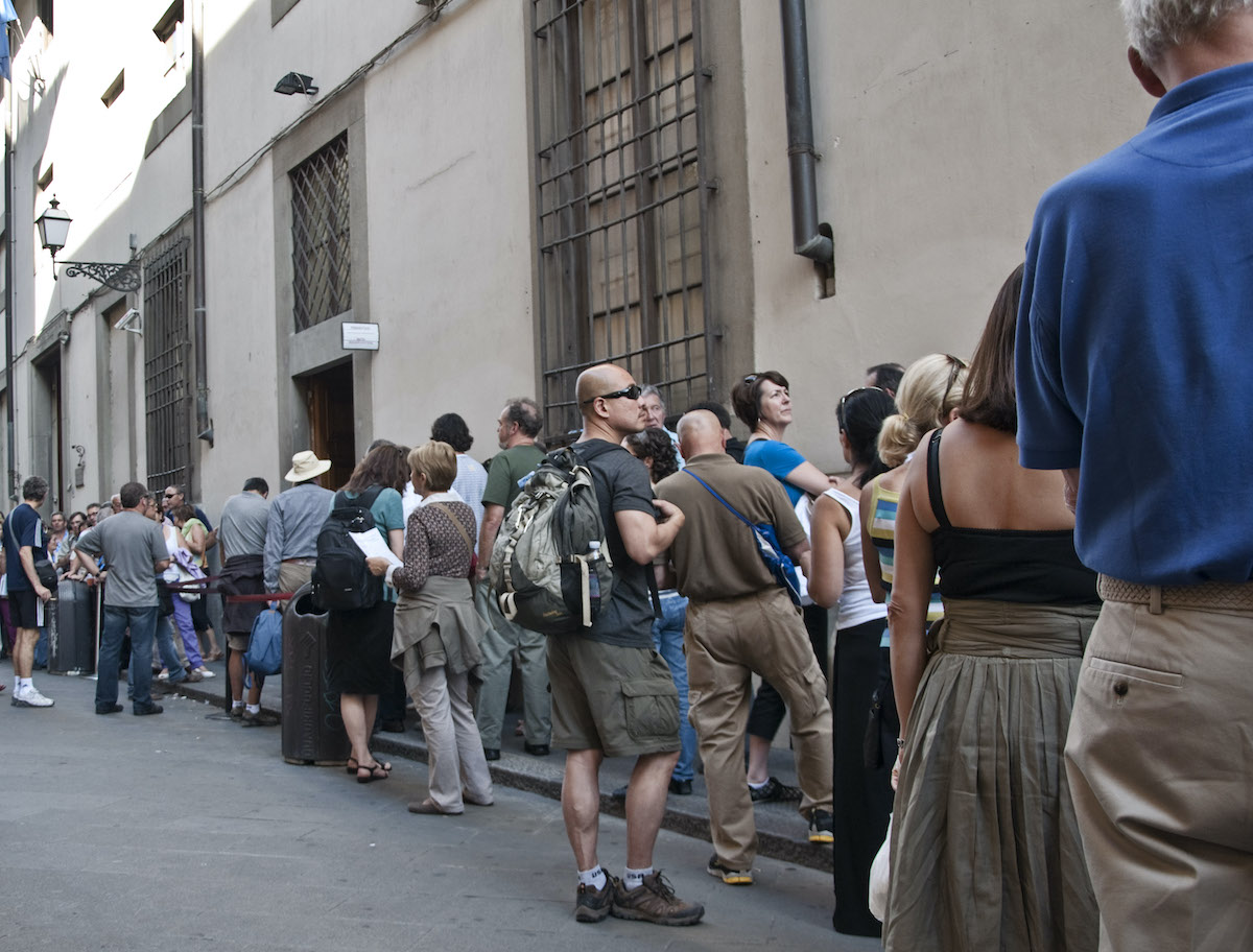 Personas esperando en una larga fila afuera de un edificio.