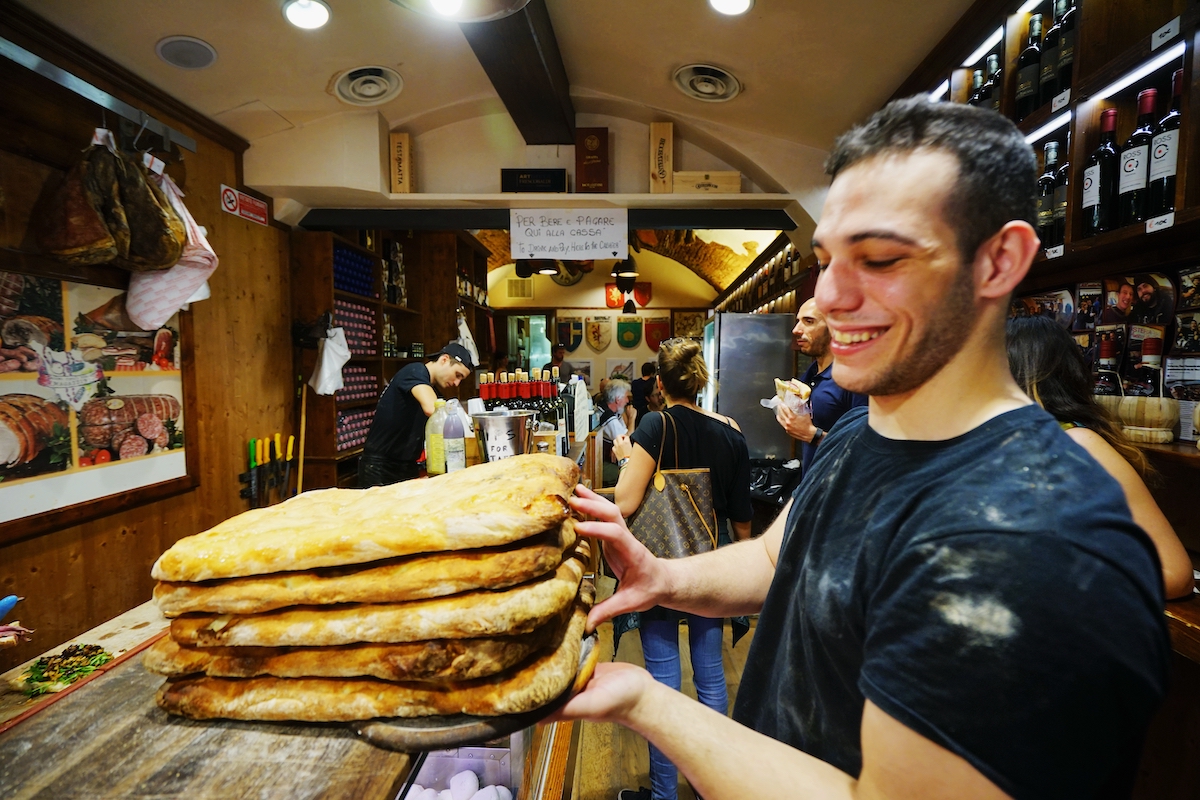 Un hombre sonriendo mientras sostiene palitos de pan estilo focaccia encima del mostrador de un restaurante