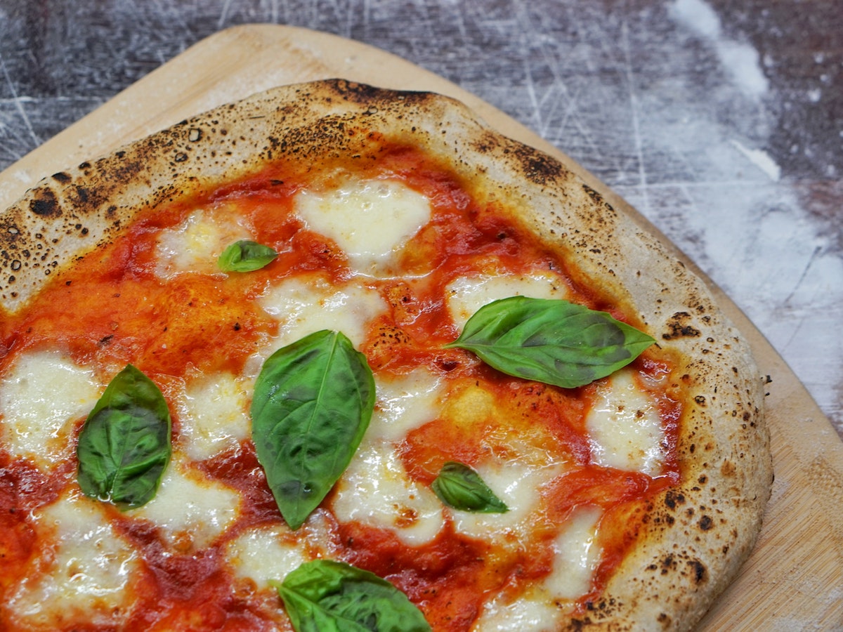 primer plano de pizza margherita, corteza marrón claro con salsa de tomate, mozzarella derretida y cubierta con hojas de albahaca fresca