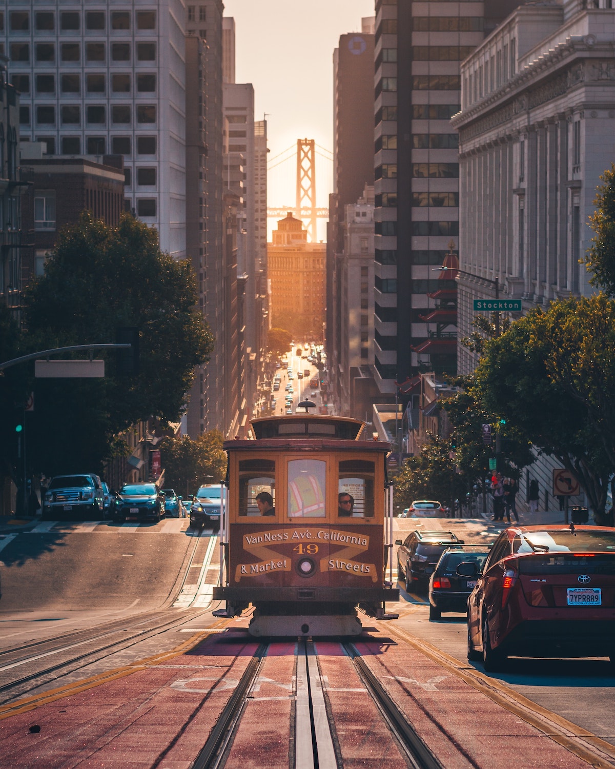 Una vista de un teleférico en una calle inclinada en San Francisco con un puente en el fondo mirando entre edificios 