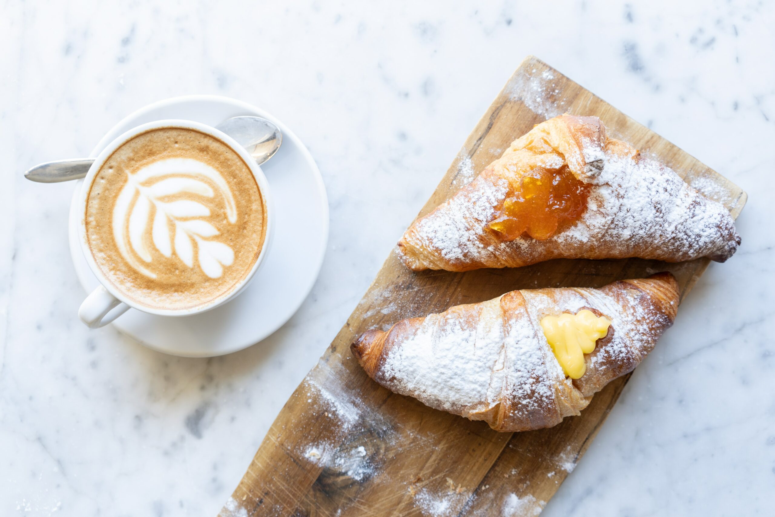 Un plato de madera con dos pasteles de cornetti italianos y un capuchino