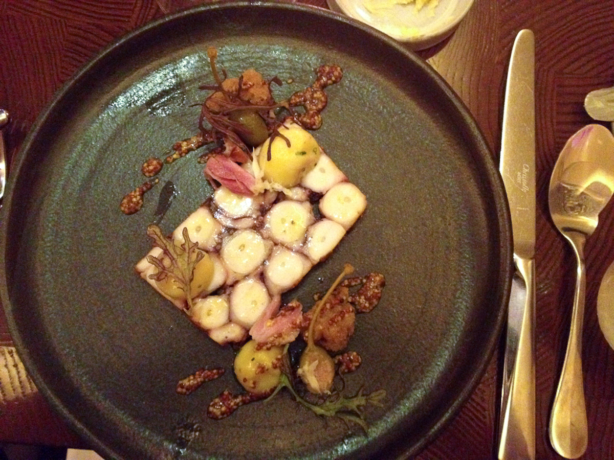 Una presentación moderna de un plato de pulpo y patata en un plato negro