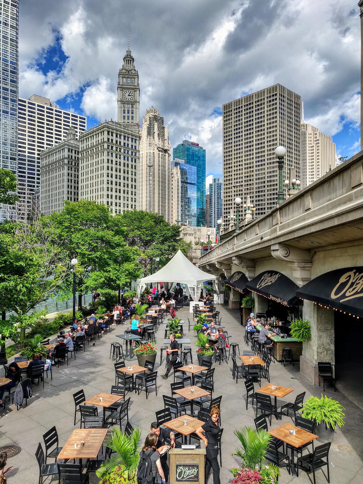 Una vista del circuito de Chicago con un restaurante con mesas al aire libre en primer plano inferior y el horizonte de la ciudad en el fondo. Hay más de 7.000 lugares para comer en Chicago.