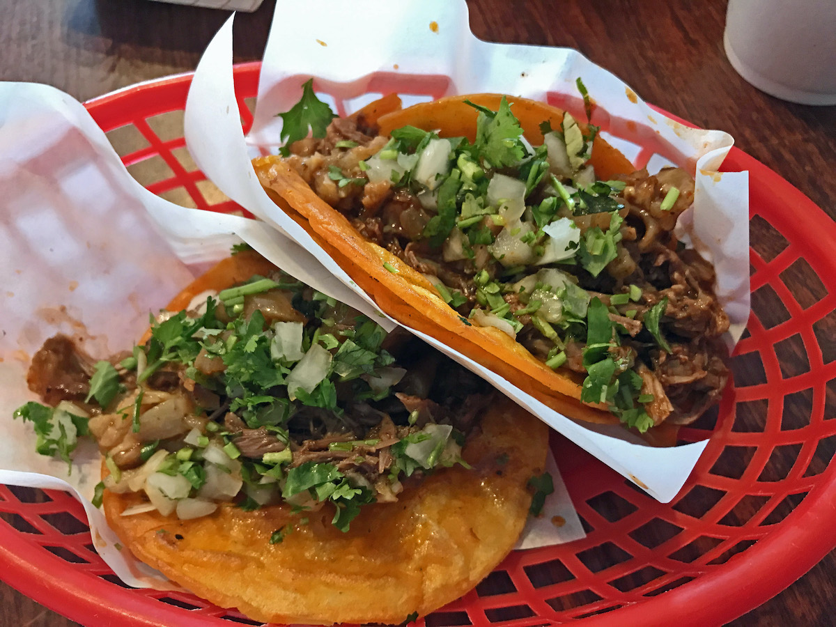 Dos tacos pequeños de carne de res, cilantro y cebolla servidos en una canasta roja