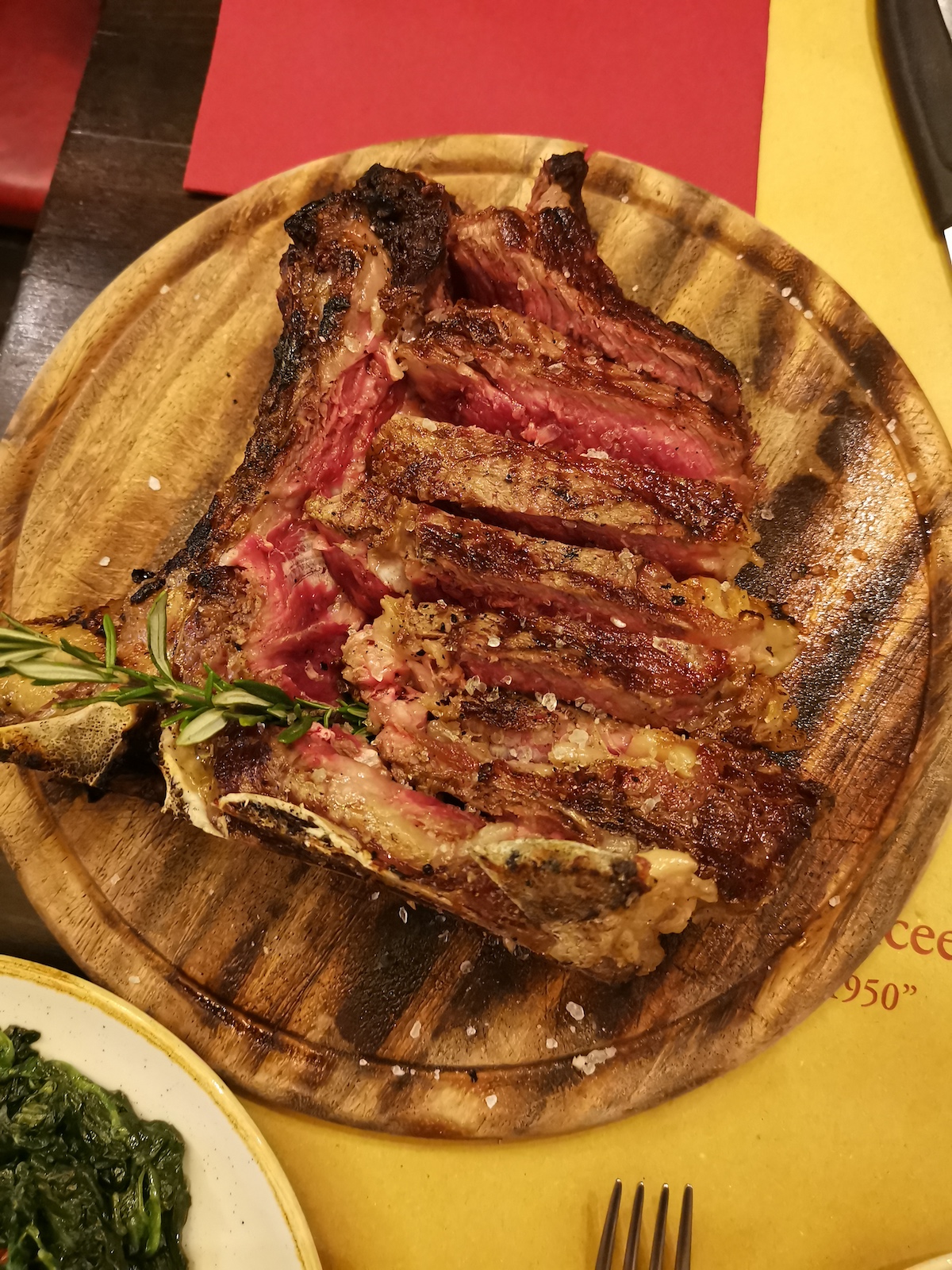 Fotografía cenital de bistec raro en rodajas en un plato de madera adornado con hierbas