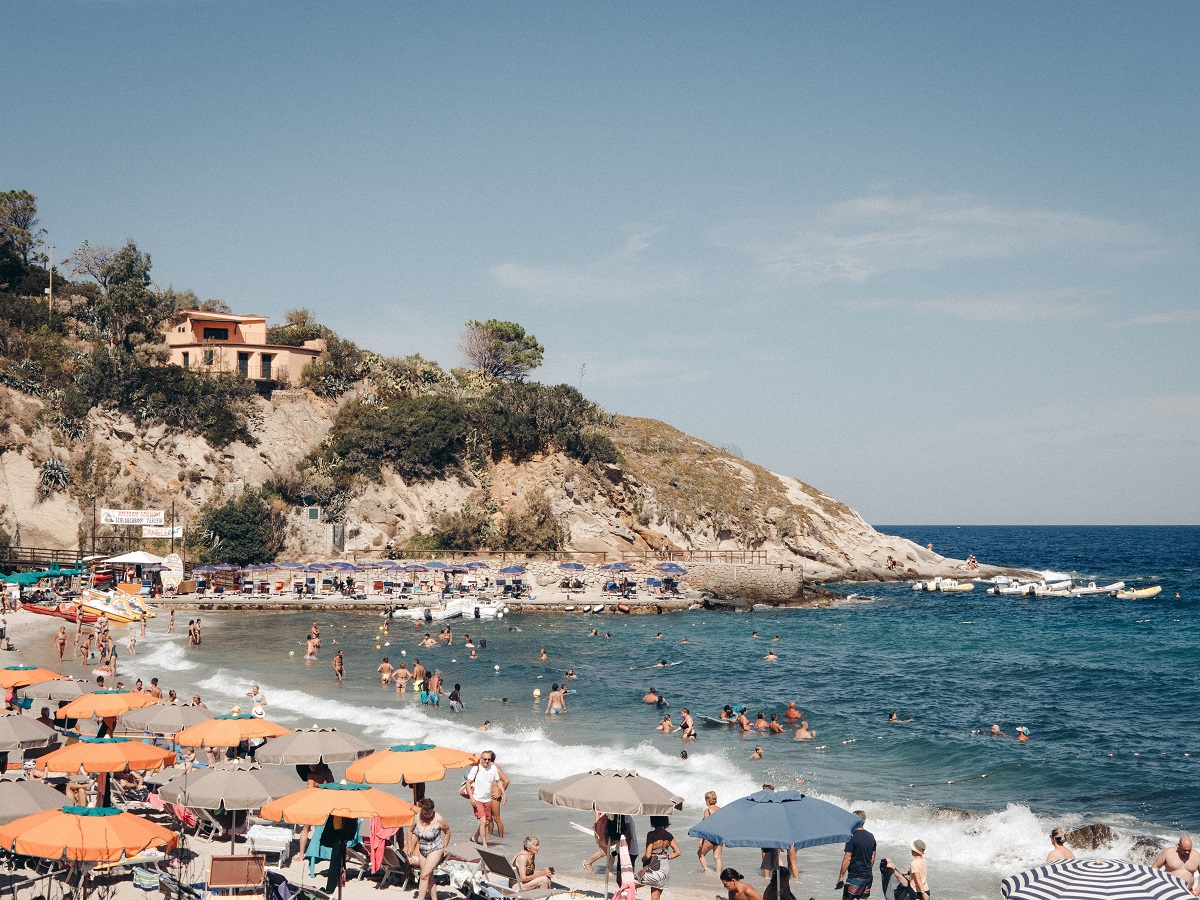 Una playa de arena blanca con agua azul con bañistas, bañistas y una pequeña colina al fondo