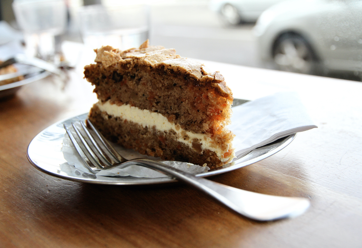Una rebanada de pastel de zanahoria con glaseado de queso crema dividiendo las capas en un plato cerca de un tenedor.