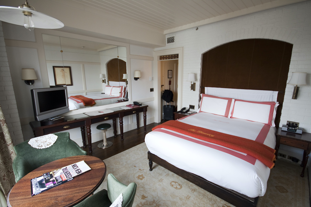 Una habitación de hotel con una cama tamaño queen con cabecera de madera y sábanas blancas con detalles en naranja