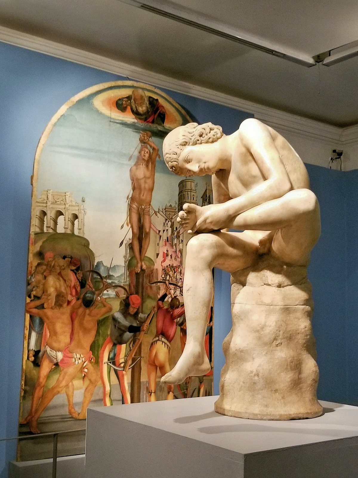 Estatua de mármol de un niño sentado sobre una columna corta, inspeccionando su propio pie