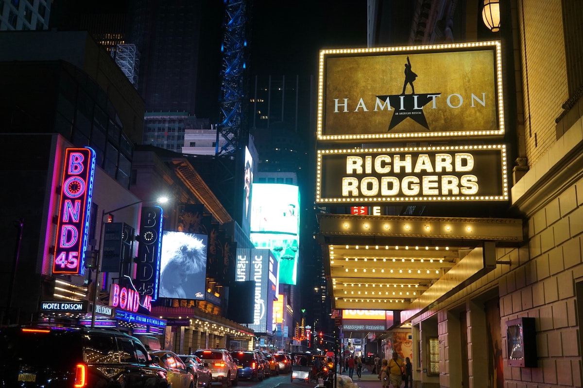 Una escena que mira hacia Broadway en Nueva York por la noche, con una marquesina para Hamilton en primer plano