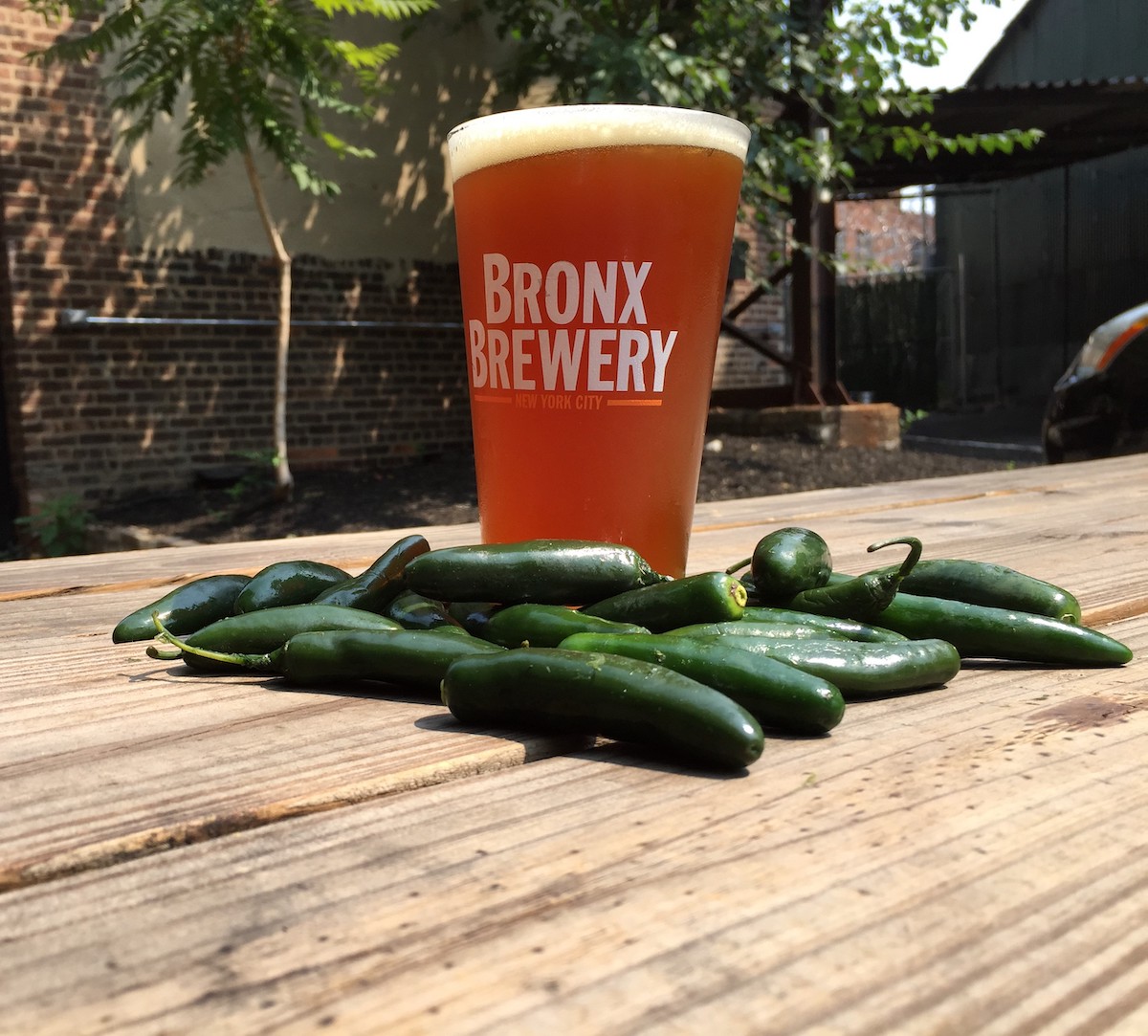 Cerveza en un vaso que dice Bronx Brewery sobre una mesa de madera con algunos pimientos verdes pequeños