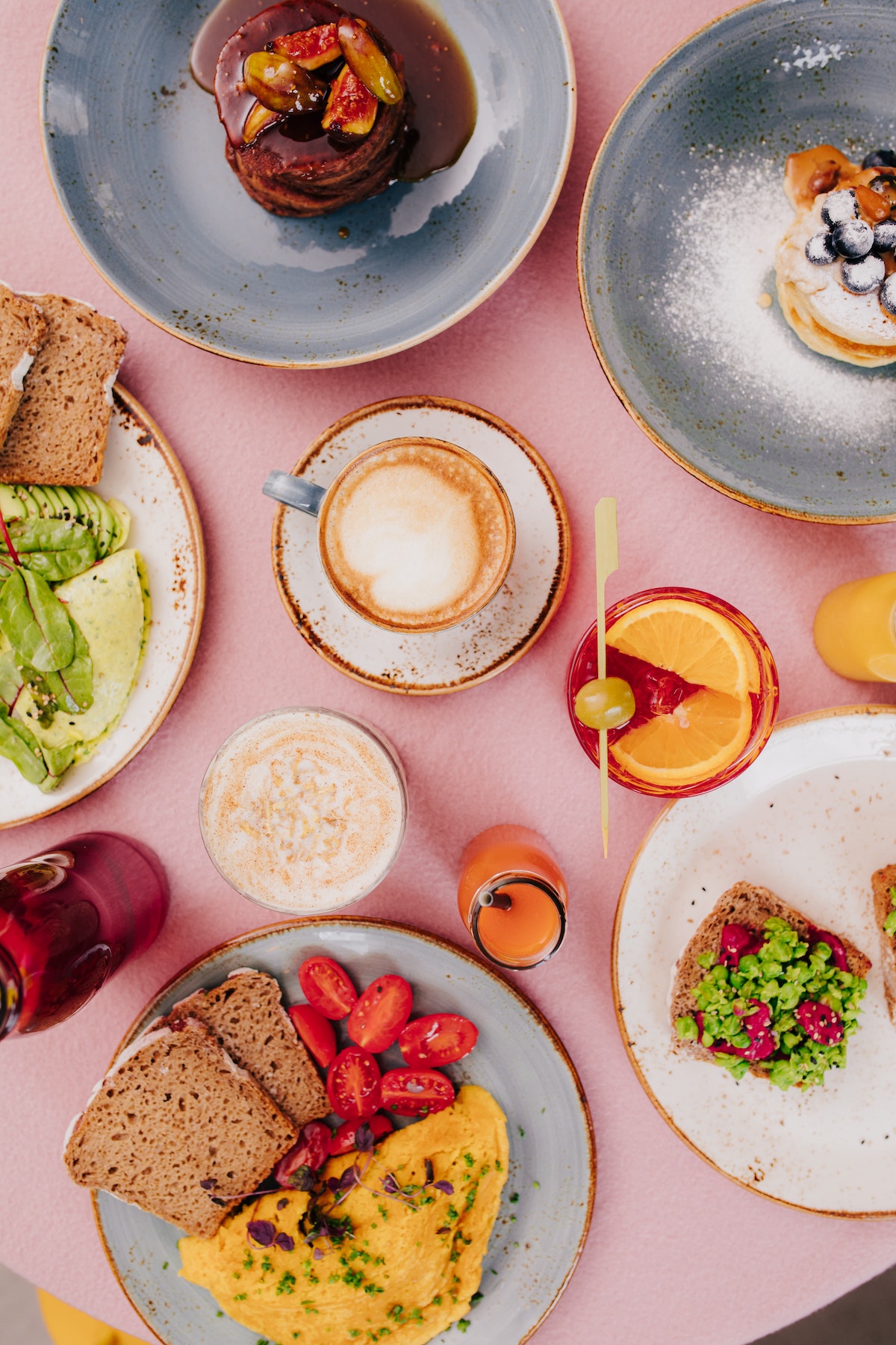 Fotografía cenital de artículos de brunch en una mesa que incluye tostadas, tortillas, cócteles y café