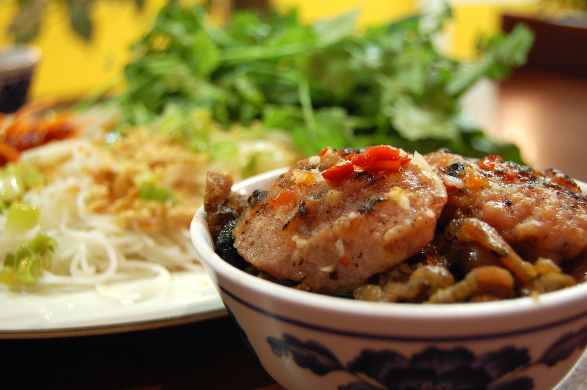 Salchichas de cerdo vietnamitas en un cuenco de cerámica con un plato de fideos vermicelli en el fondo.
