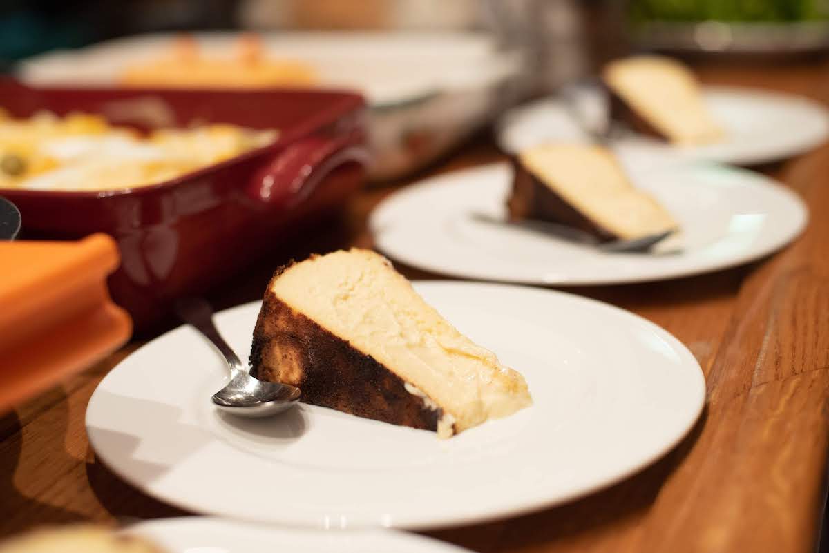 Tres rebanadas de pastel de queso crema en platos blancos alineados sobre una superficie de madera