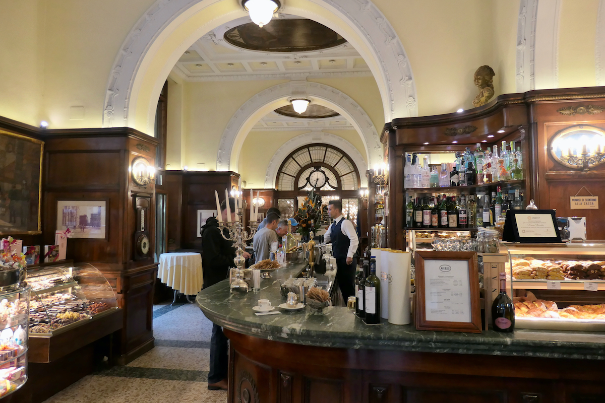 Interior de un café histórico en Florencia, Italia, con altas puertas arqueadas y paneles de madera oscura.