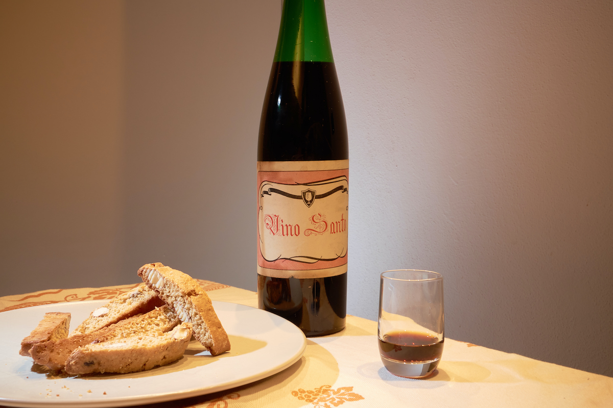 Un plato de galletas tipo biscotti en una mesa al lado de una botella y una pequeña copa de vino dulce.