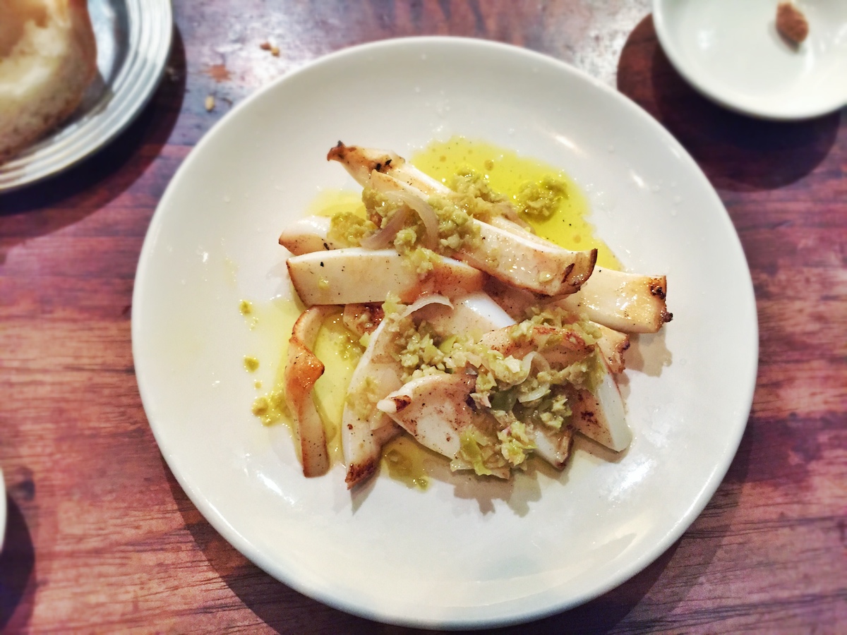 Filete de pescado a la parrilla con limón en conserva, trozos de aceitunas verdes y vinagreta de chalota en un plato blanco redondo