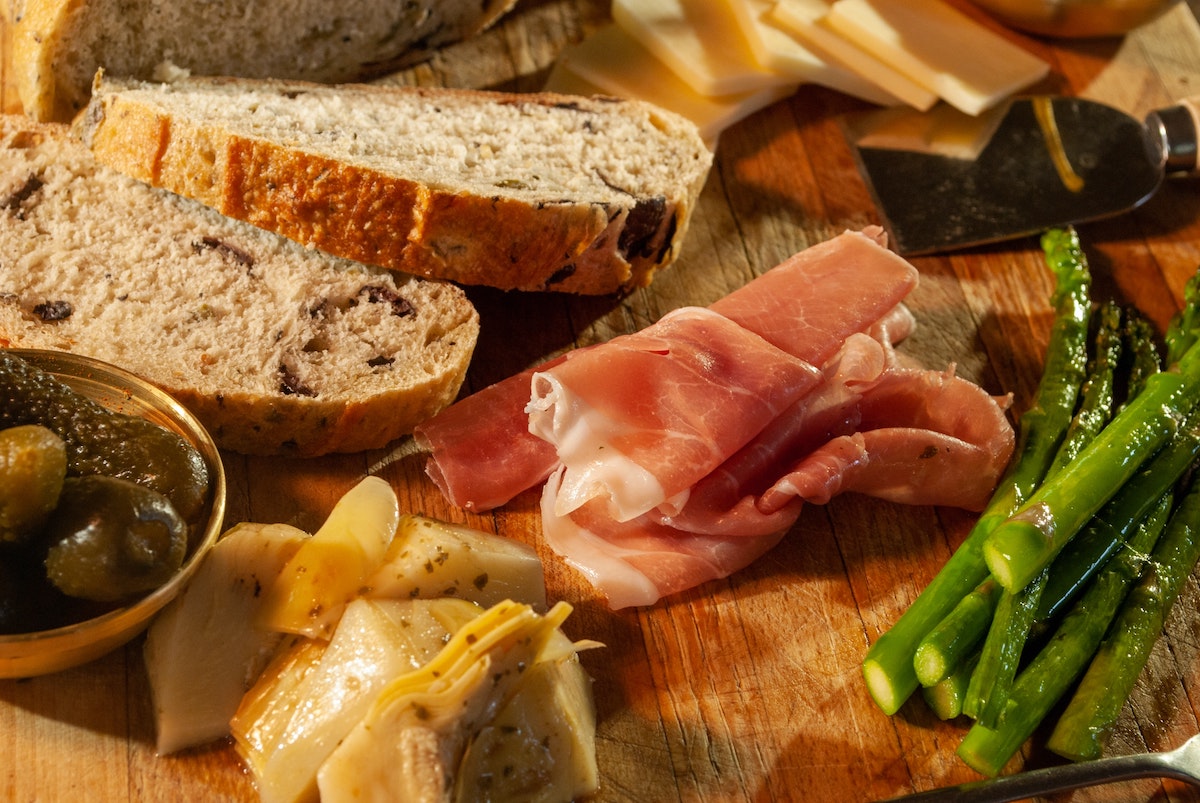 Prosciutto, aceitunas, espárragos, queso y pan en una tabla de servir de madera