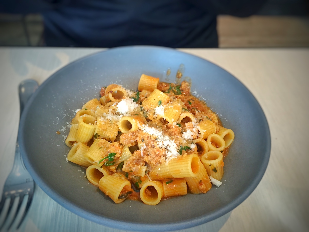 Pasta Rigatoni con azafrán, hierbas frescas y queso en un plato azul.