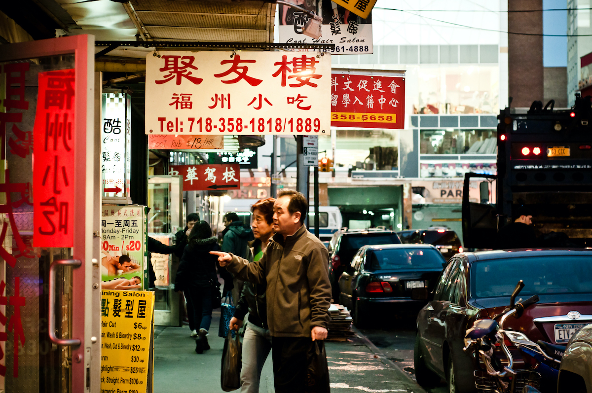 Una pareja china mirando carteles fuera de un escaparate en Chinatown, Queens