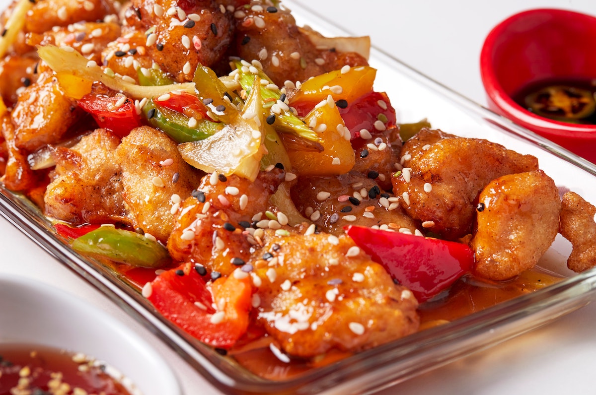 Plato de pollo chino con pimientos y semillas de sésamo en un plato de cristal