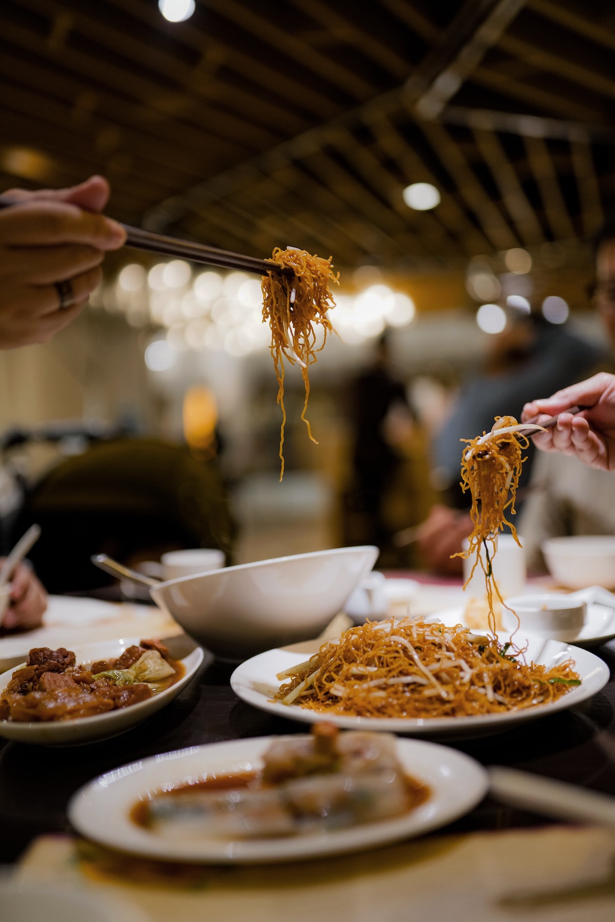 Gente comiendo fideos de platos blancos con palillos