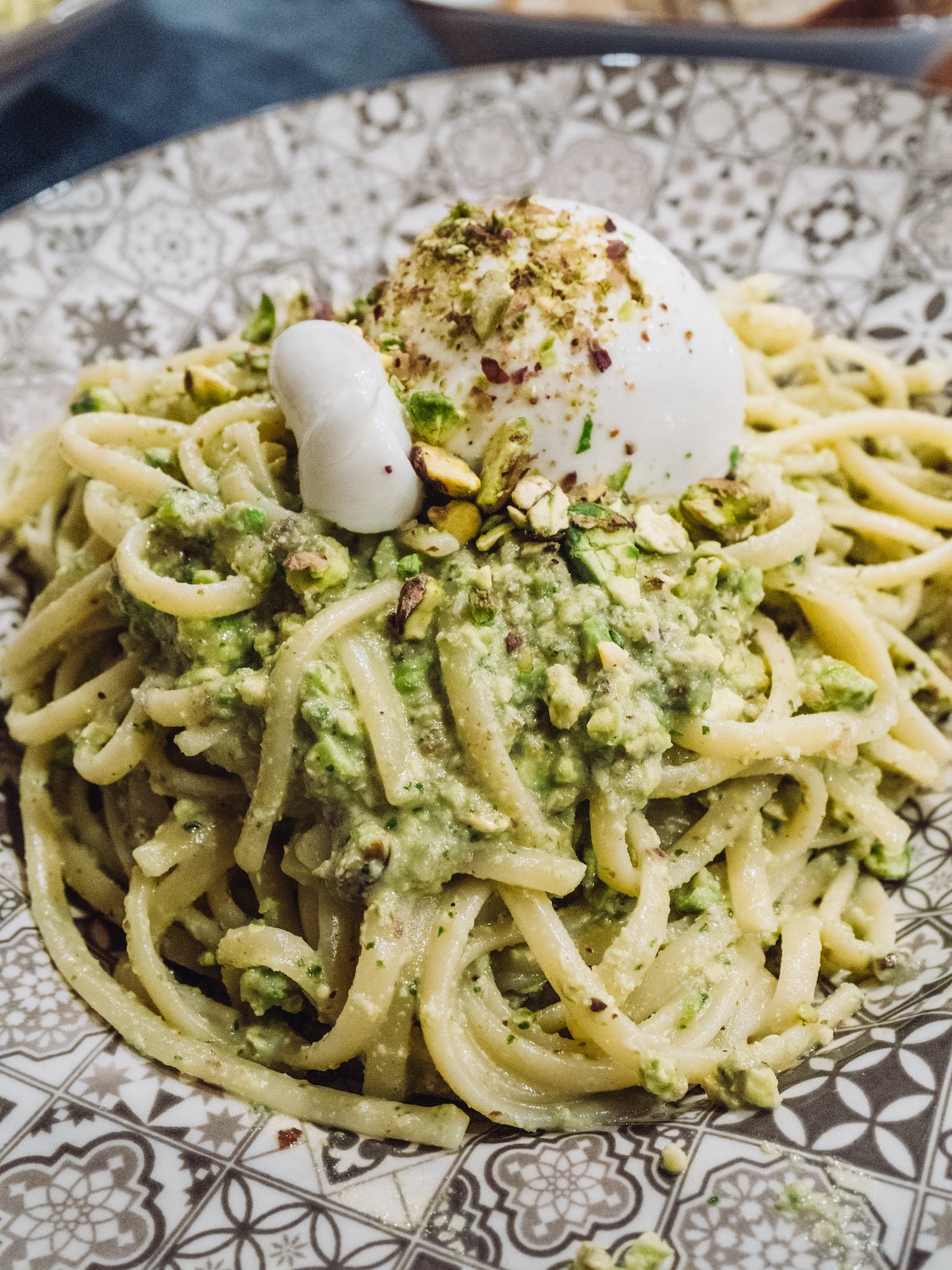 Primer plano de un plato de pasta vegetariana con pistachos y queso burrata.