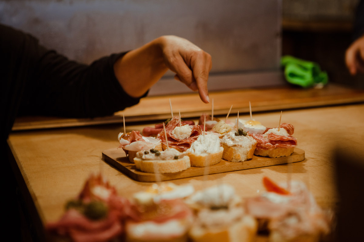 Se sirven pequeños bocados en pequeños trozos de pan colocados encima de una tabla de madera, con la mano apuntándolos.
