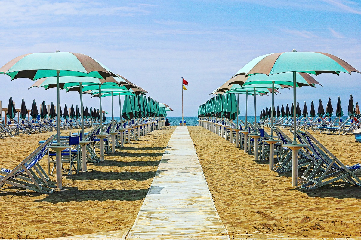 Una playa de arena llena de sillas de playa con sombra y un camino que conduce al agua