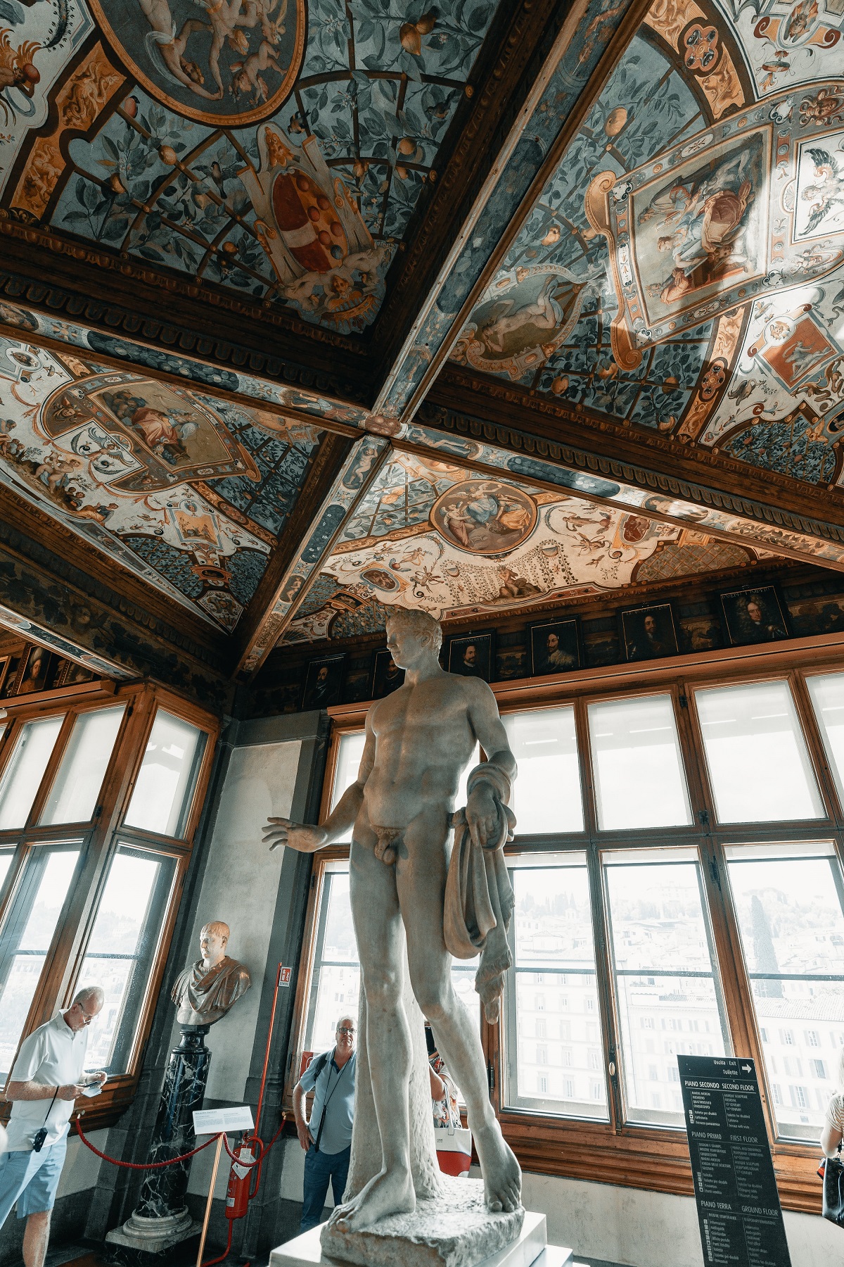 Una estatua de marbe vista desde abajo en un museo con un techo pintado de manera intrincada