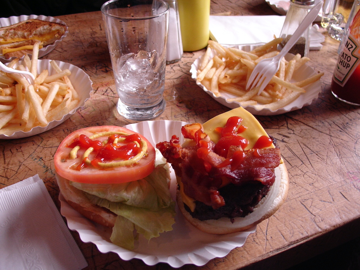 Hamburguesa abierta con lechuga, tocino, tomate y ketchup servida en un plato de papel blanco.
