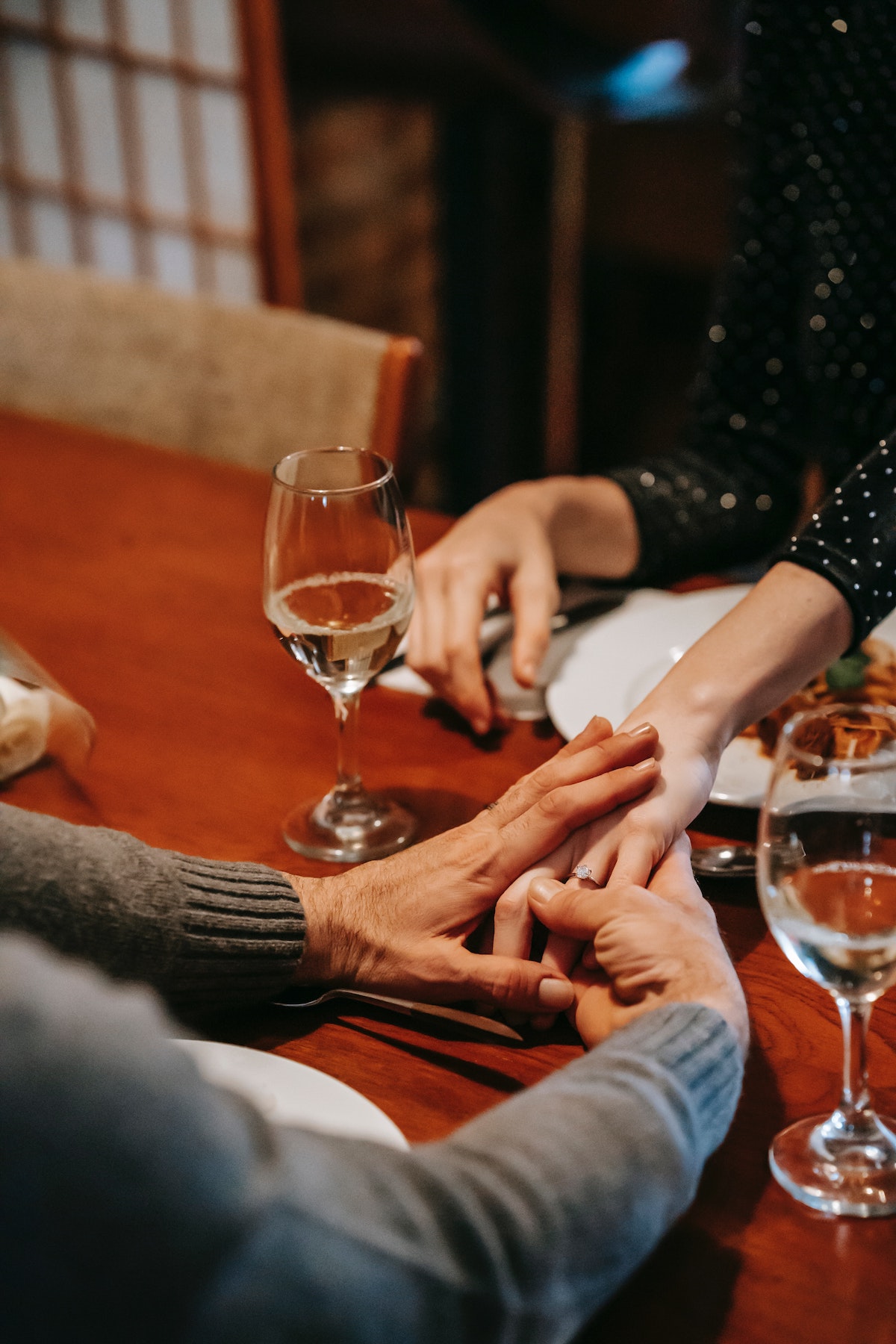 Cerca de una pareja tomados de la mano en una mesa roja con copas de vino a ambos lados.