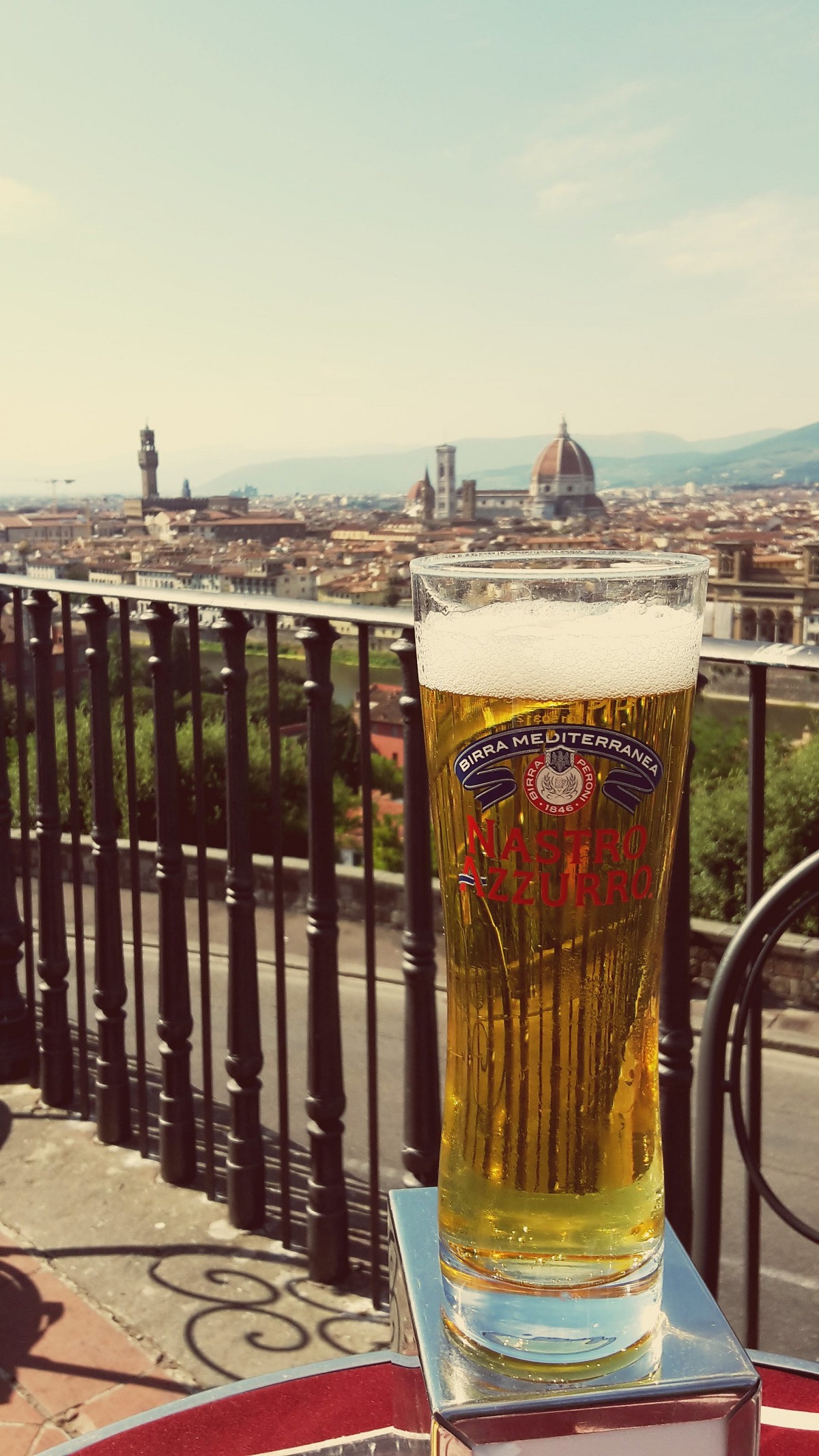 Un vaso largo y alto de cerveza pálida en primer plano y el Duomo de Florencia al fondo