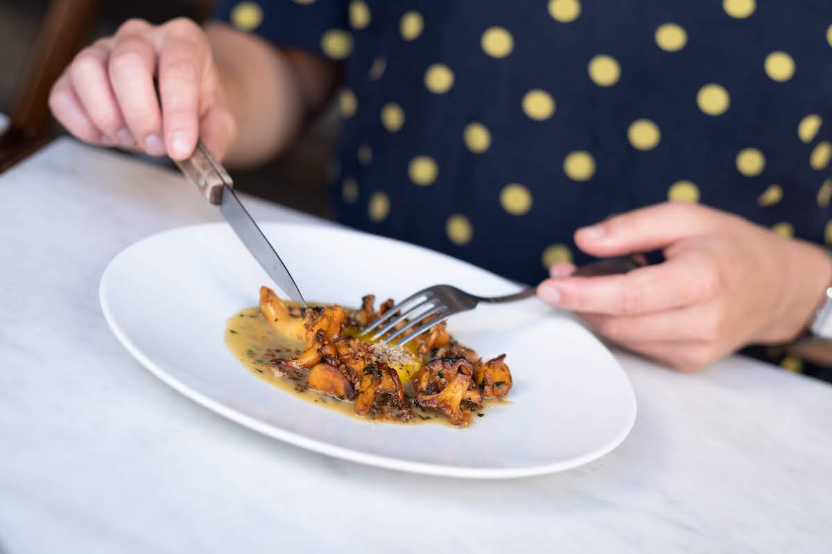 Cerca de las manos de una persona cortando comida en un plato blanco