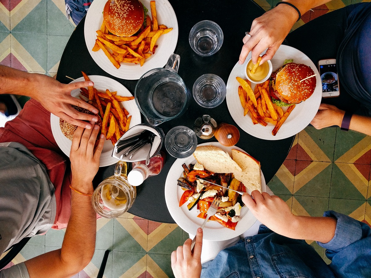 Vista de comensales comiendo hamburguesas, papas fritas y verduras desde arriba en una mesa de restaurante