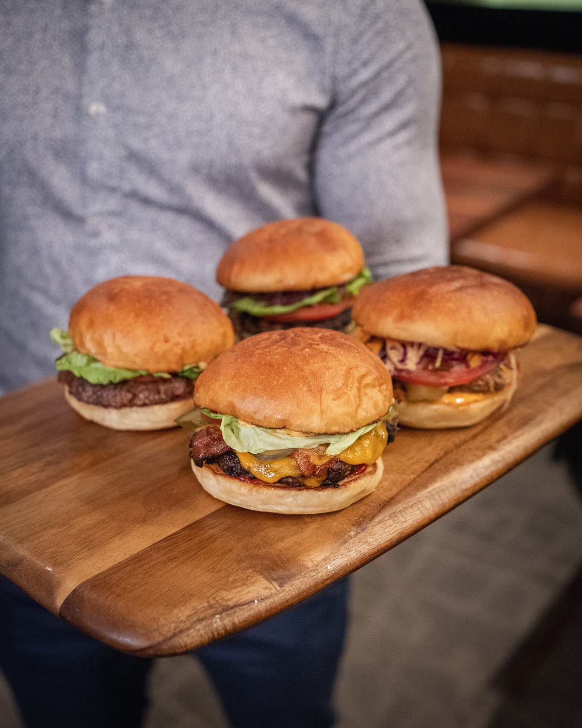 Un hombre que sostiene una mesa de madera con 4 hamburguesas.
