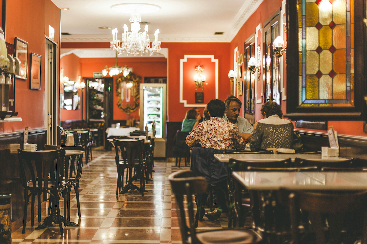 Interior de un salón de té ornamentado con paredes rojas, candelabros de cristal y mesas de mármol.