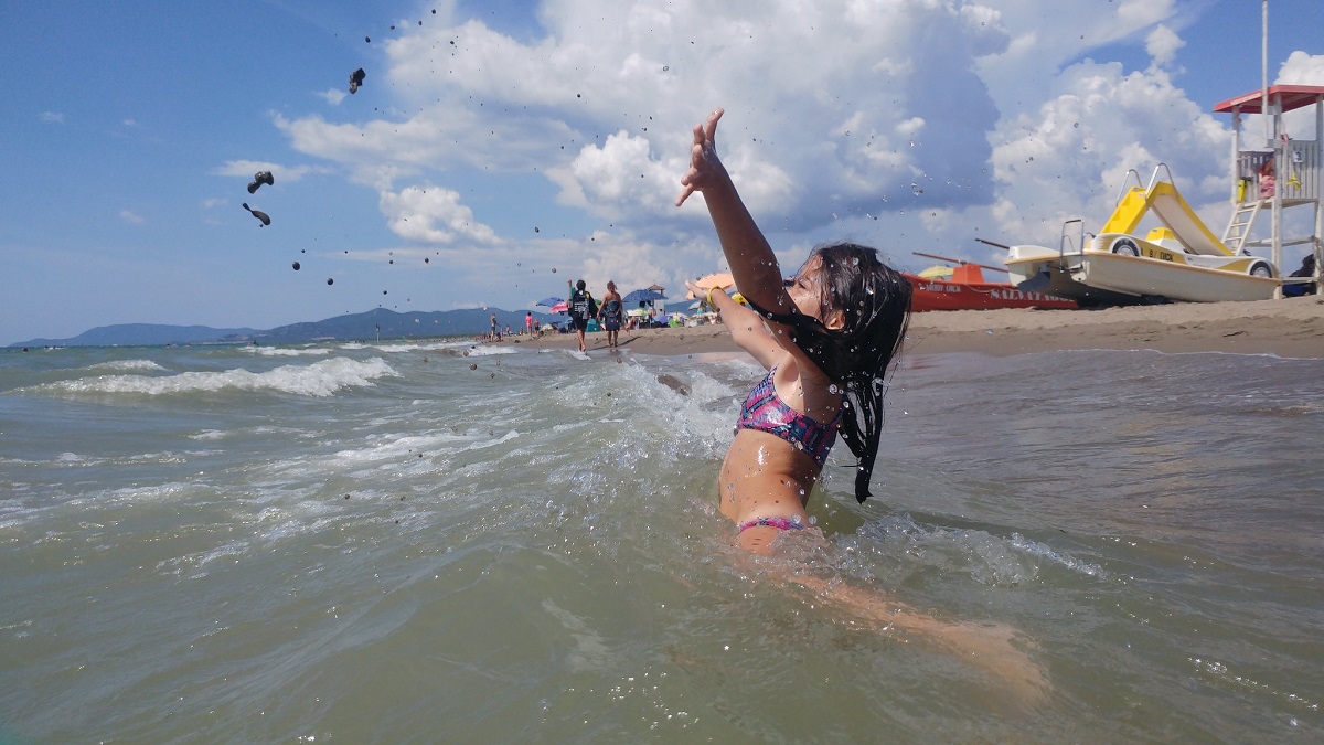 Una niña nadando en la playa soplando arena en el aire