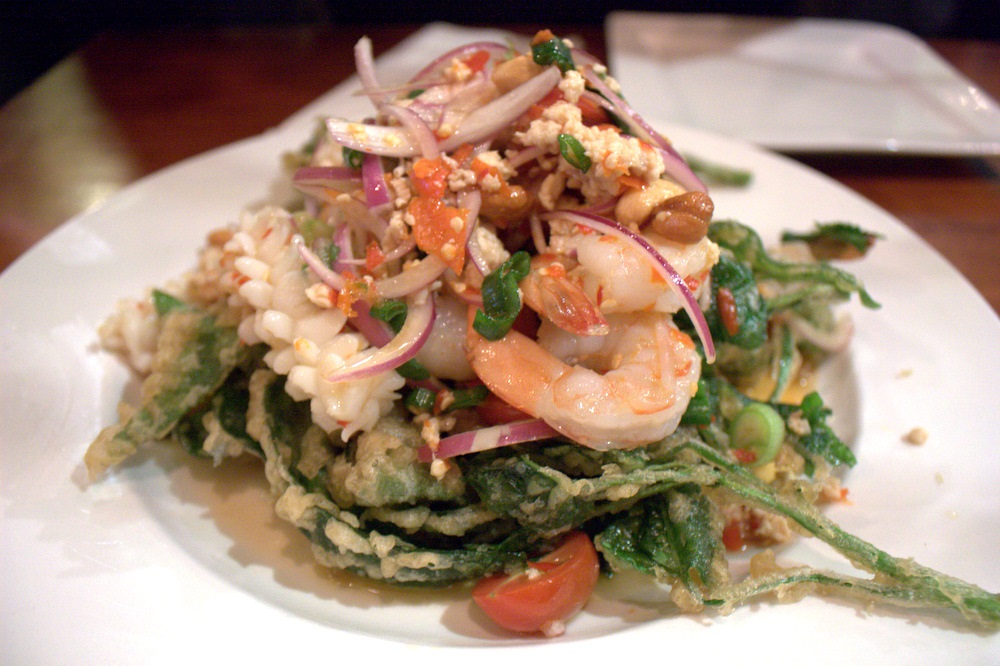 Ensalada verde con verduras fritas, mariscos, camarones y cebollas rojas en un plato blanco