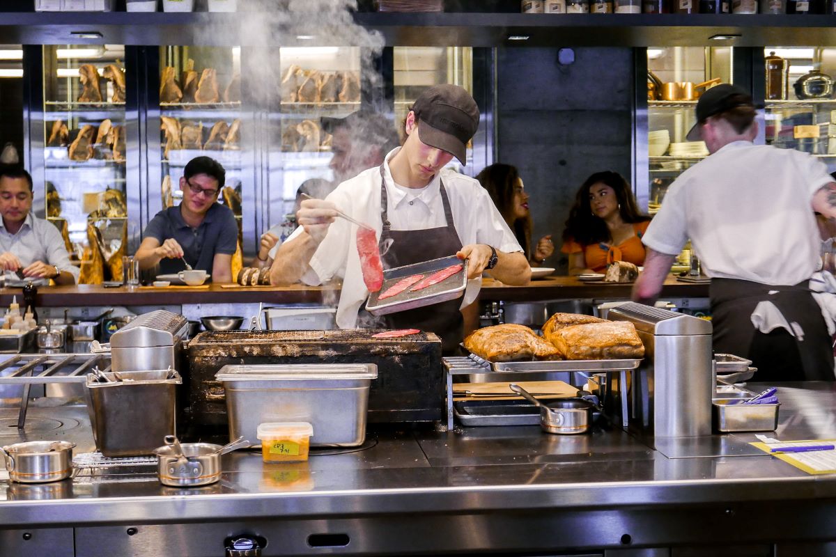 un hombre preparando carne a la parrilla en la cocina abierta