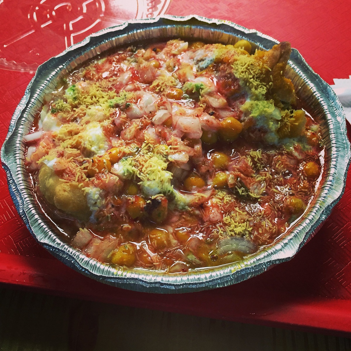 Un recipiente de plata para llevar lleno hasta los topes de comida india hecha con samosas y salsa roja