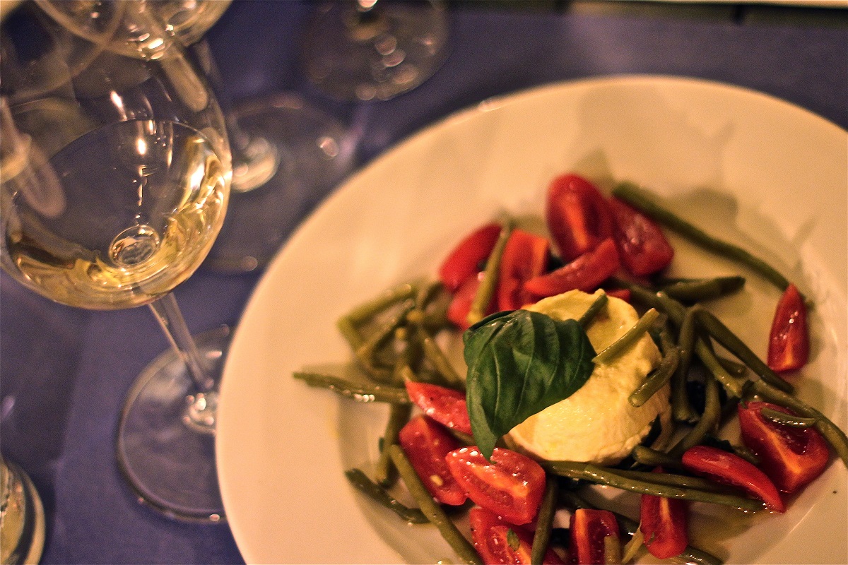 Un plato de judías verdes, tomates diminutos y burrata con una copa de vino blanco
