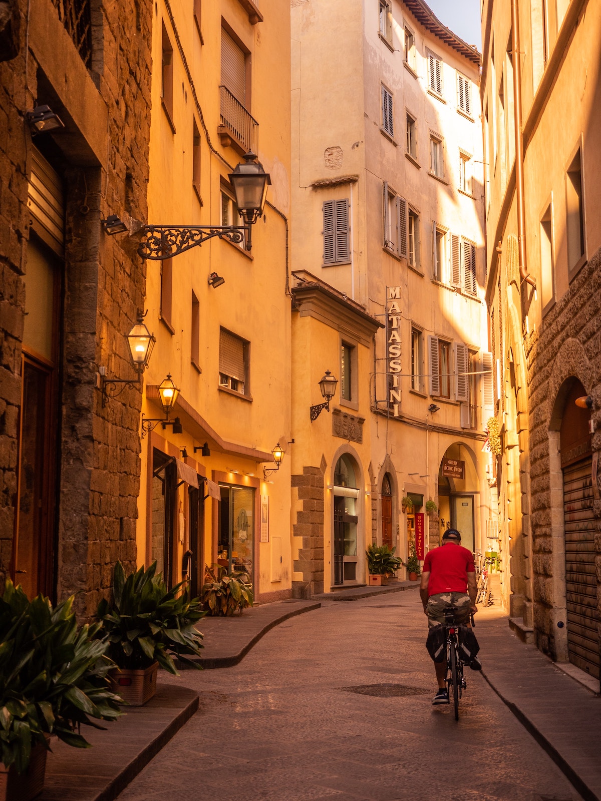 Una persona con una chaqueta roja montando una bicicleta en una calle peatonal de Florencia