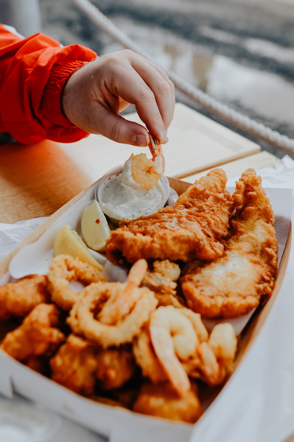 Una persona comiendo pescado frito de una caja y mojando un trozo de camarón en salsa blanca