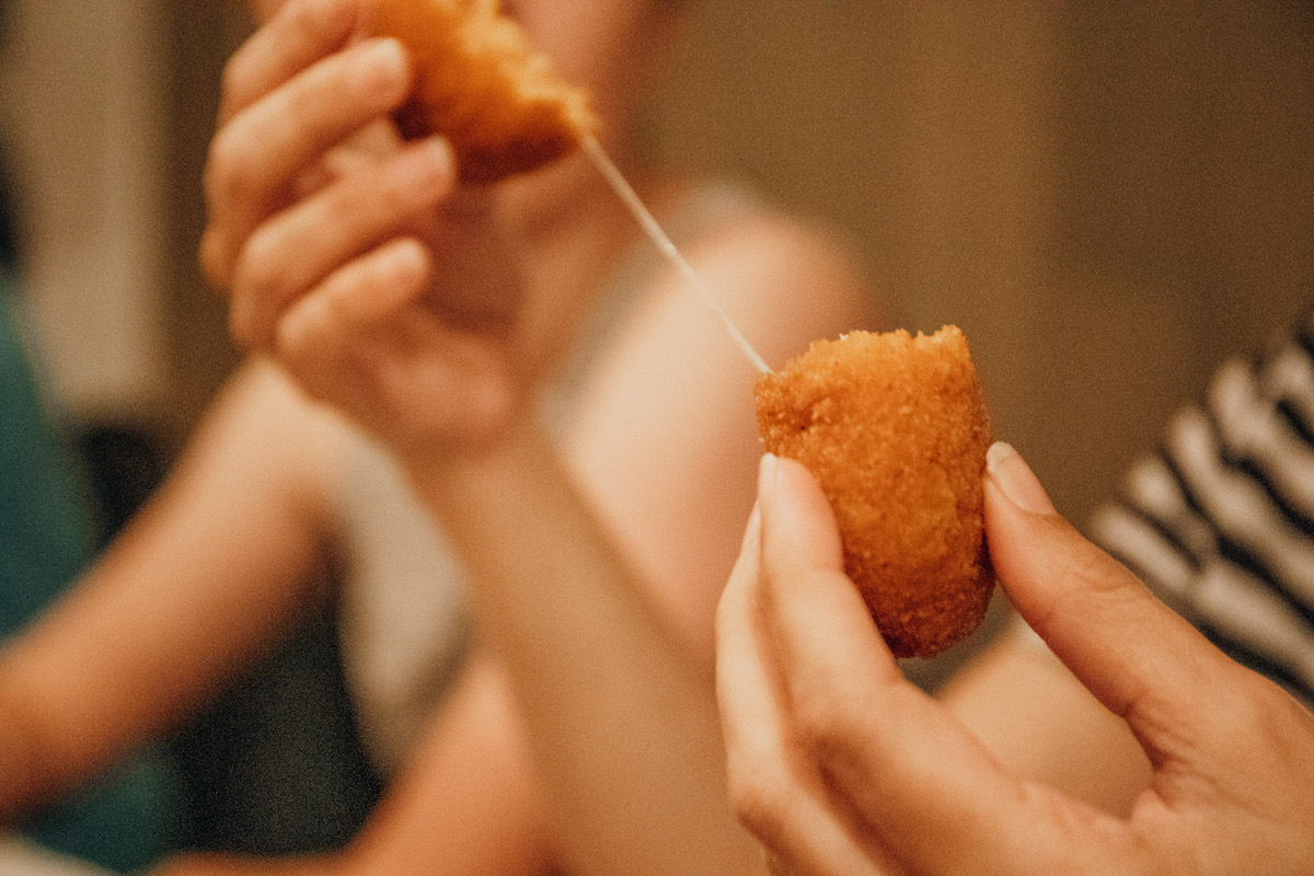 Alguien parte una croqueta frita por la mitad para soltar un hilo de queso derretido.